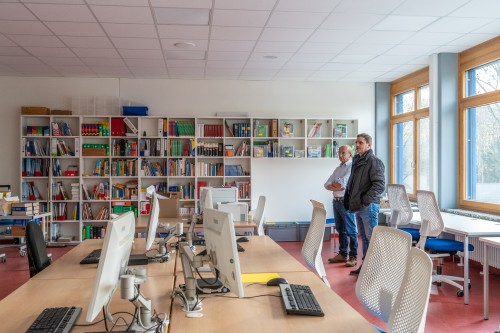 Blick in die Lehrerbibliothek mit PC-Arbeitsplätzen und Bücherregalen. Rechts stehen Schulleiter Spinner und Michael Heitzmann                                                                                                        