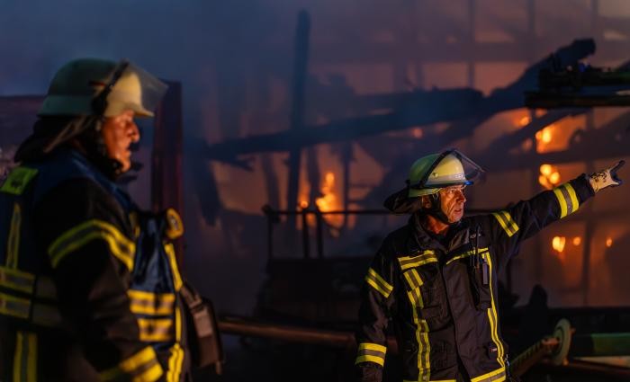 Zwei Feuerwehrmänner vor dem brennenden Ökonomiegebäude