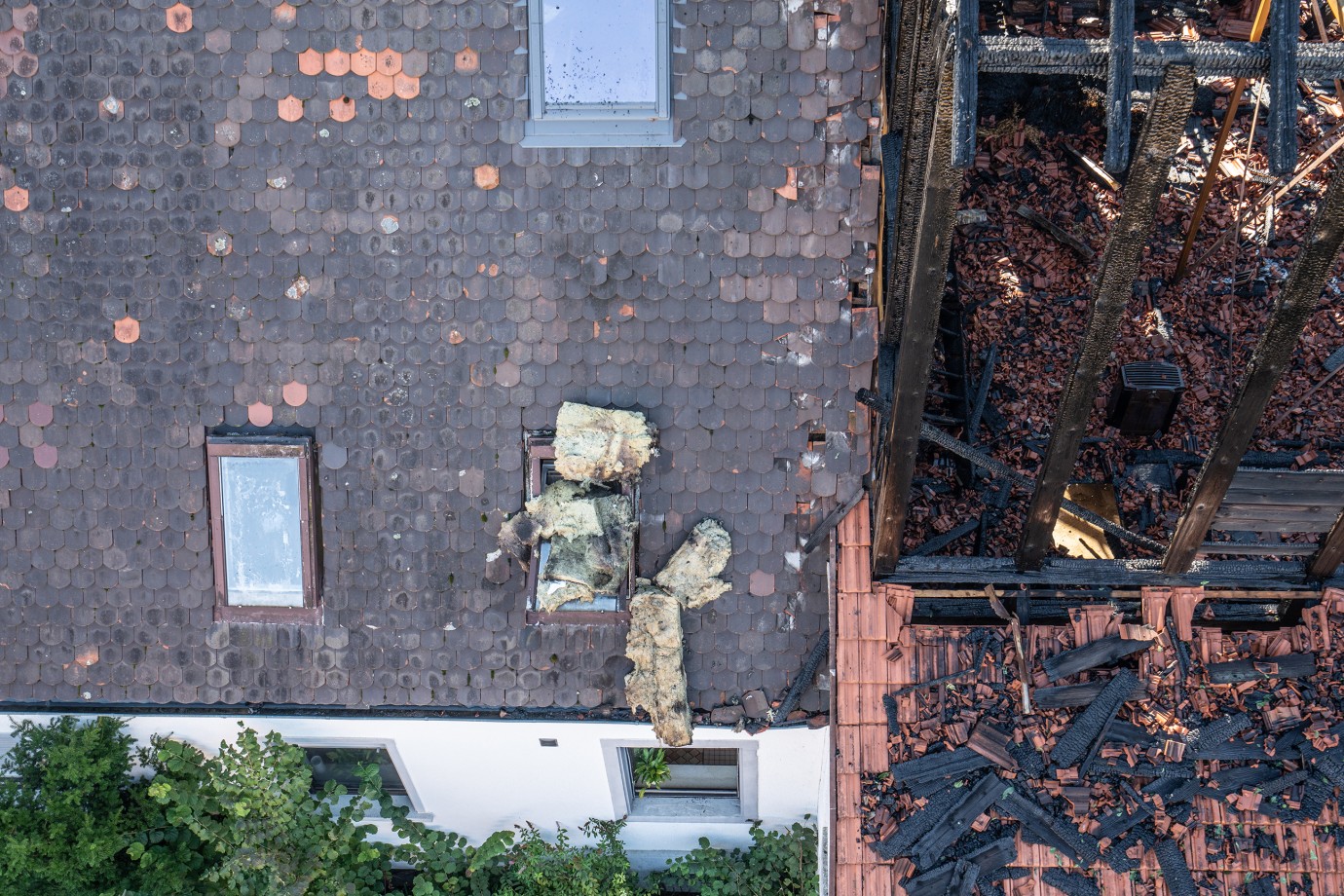 Blick auf das Dach des Wohnhauses, das nur am Rande beschädigt ist und die direkt angrenzende verkohlte Brandruine               