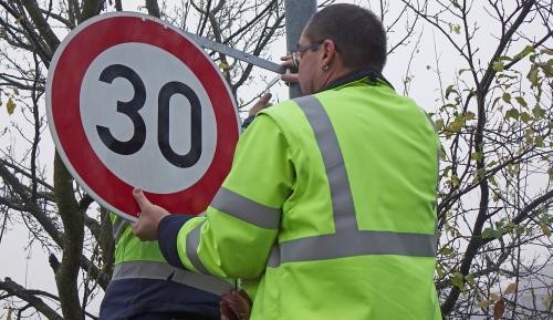 Mitarbeiter des Betriebshofs montieren ein Straßenschild, das Tempo 30 ausweist.
