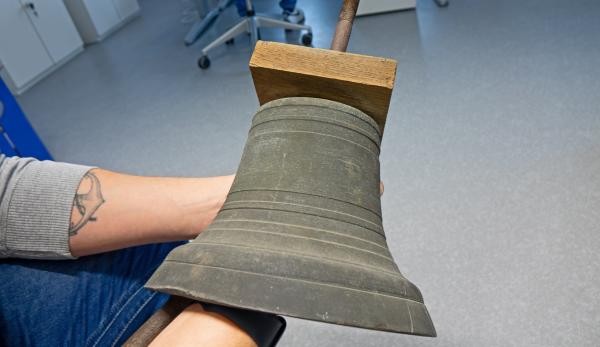 Ein Mitarbeiter des Gebäudemanagements hält die schwere Messingglocke.