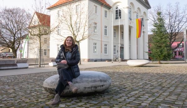 Sprachpool Sprachvermittlerin Nesrin Demirkiran sitzt auf einem Stein vor dem Rathaus.