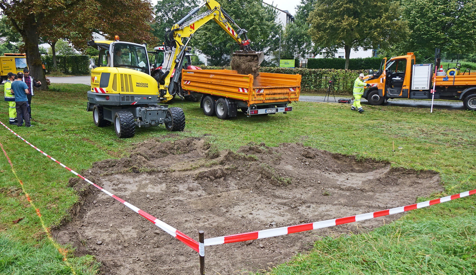 Ein Bagger gräbt den Boden auf und kippt das Erdreich in einen Anhänger.